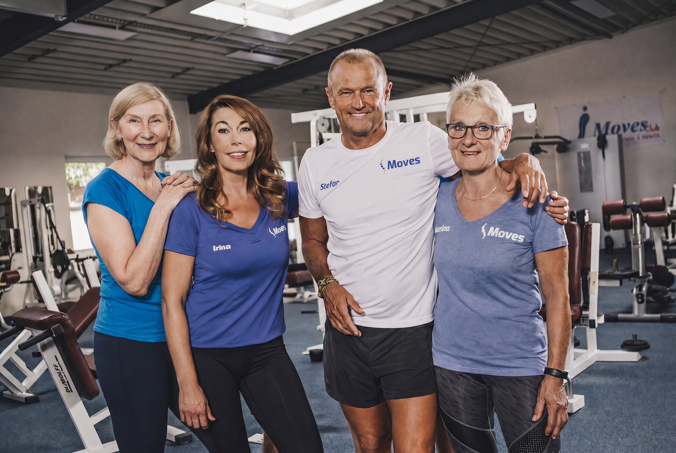 Vier Personen in sportlicher Kleidung lächeln in einem Fitnessstudio in die Kamera.